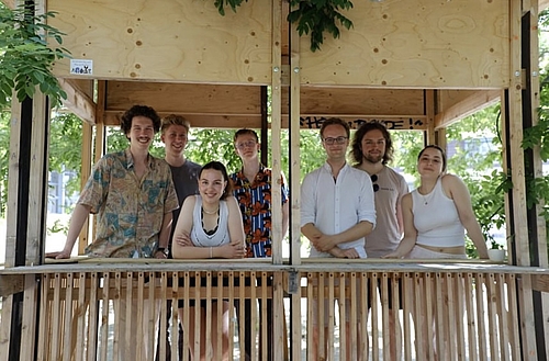 Das Bild zeigt eine Gruppe von jungen Menschen in einem Holz-Pavillon.